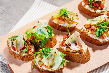 Italian bruschetta with salmon, tomatoes, cheese and basil pesto on a grey concrete or stone background.