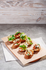 Italian bruschetta with salmon, tomatoes, cheese and basil pesto on a grey concrete or stone background.