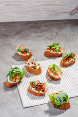 Italian bruschetta with salmon, tomatoes, cheese and basil pesto on a grey concrete or stone background.