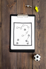 Sport coach concept. Pad with tactic plan of the match near whistle and football ball on wooden background top view copy space