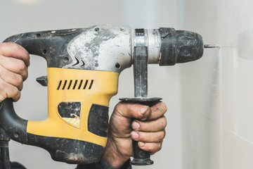 A drilling machine is making a hole on a wall of tiles. The worker has big hands and the machine is...