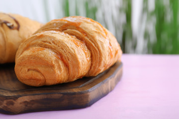 Wooden board with tasty croissants on table