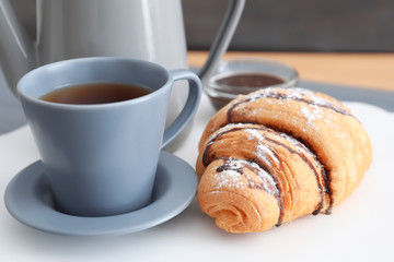 Tasty croissant near cup of coffee on table