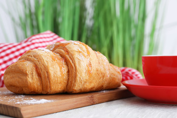 Wooden board with tasty croissant on table