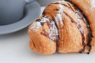 Tasty croissant with chocolate syrup on table, closeup