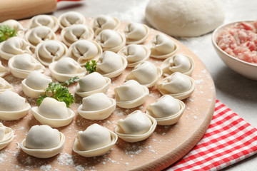 Wooden board with raw dumplings on table
