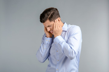 Young man suffering from headache on grey background