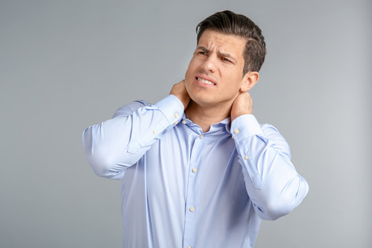 Young man suffering from neck pain on grey background