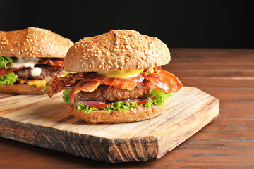 Tasty burgers with bacon on wooden board