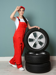 Obraz na płótnie Canvas Female mechanic in uniform with car tires on color wall background