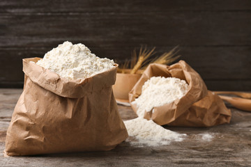 Paper bags with flour on wooden table
