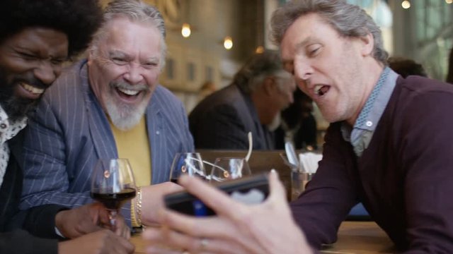 Mature group of men in a wine bar looking at a cell phone together and laughing