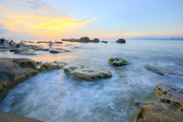 Dramatic dawning sky with golden clouds over the rocky coast ~ Scenery of rising sun illuminating the sea water at a rocky beach ( Long Exposure Effect )