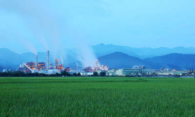 View of a factory in the middle of a green farmland in the early morning twilight ~ Factory pipes polluting air in a silent morning, a serious environmental issue
