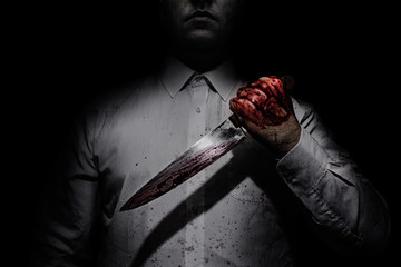 Photo of a killer in white shirt holding a bloody knife on black background with upper lighting. - obrazy, fototapety, plakaty