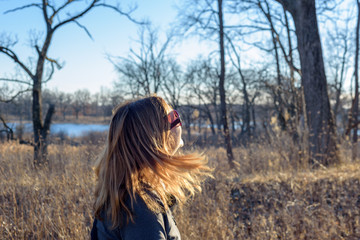 woman walking in woods with blonde hair blowing in sunshine