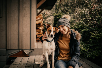 Girl with her puppy sitting outside forest cabin