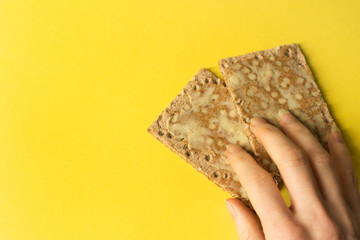 Close-up of hand grabbing two rye crackers with butter - on bright background - minimal- copy space