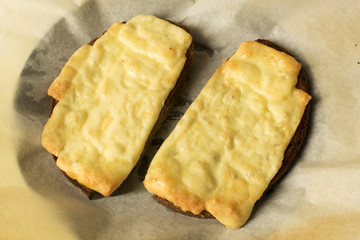 Two slices of grilled cheese on toasted rye bread  on baking paper - snack, melted cheese
