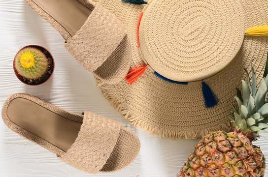 Womens summer accessories (straw hat, flip flops), pineapple, cactus on white wooden background. Fashion look, travel and summer concept. Flat lay. Natural organic stuff