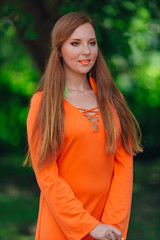 Beautiful romantic red hair girl in orange dress with long feather earrings outdoors.