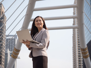Portrait of Asian business woman holding laptop with urban scene background.