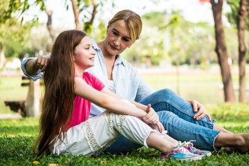 Fototapeta premium Mother and daughter relaxing sitting on grass in a park. Family and lifestyle concept