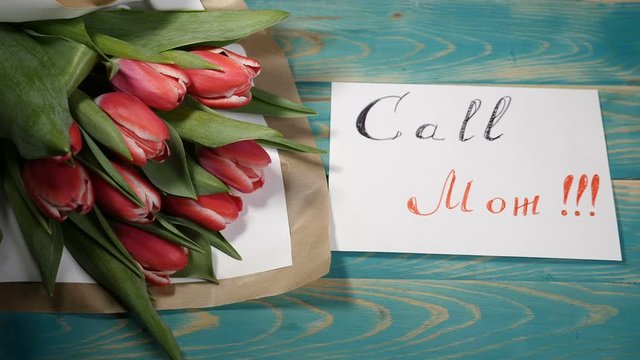 Top view of a Call Mom message note and Tulips flowers bouquet on a wooden table. Love relationship concept. Mother day. Shot in 4 k