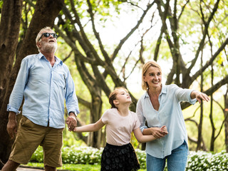 Happy family having fun together in the garden. Father, mother and daughter holding hands and walking in a park. Lifestyle concept