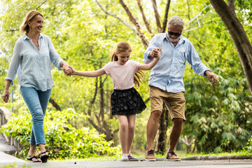 Happy family having fun together in the garden. Father, mother and daughter holding hands and walking in a park. Lifestyle concept