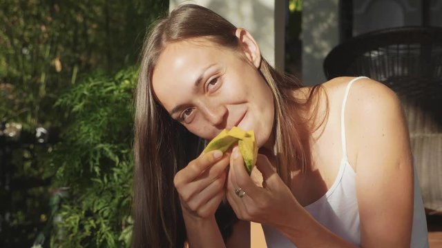 Portrait of happy young woman eats mango with pleasure at green garden
