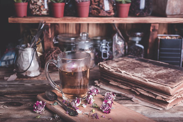 Rose buds tea, tea cup, strainer and glass jar with rosebuds. Vintage composition on a wooden table. Selective focus.