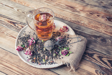 Obraz na płótnie Canvas Rose buds tea, tea cup, strainer and glass jar with rosebuds. Selective focus.