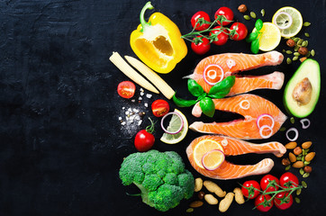 Uncooked salmon fish fillet with aromatic herbs, onion, avocado, broccoli, pepper bell, vegetables on dark background, top view. Ingredients for cooking. Banner