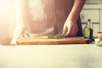 Woman hands cutting fresh green rosemary on wood chopping board in white kitchen, interior. Copy space. Homemade food conceplt, healthy recipe. Take me to work