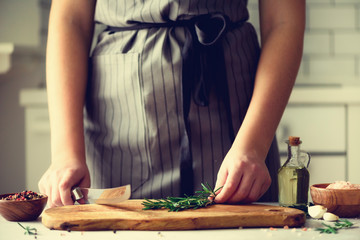 Woman hands cutting fresh green rosemary on wood chopping board in white kitchen, interior. Copy space. Homemade food conceplt, healthy recipe. Take me to work