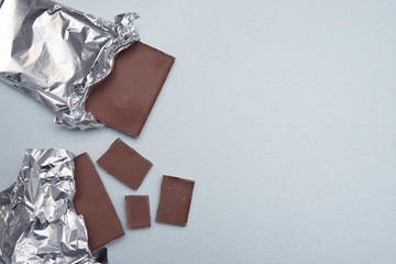 Chocolate Bar Tablet with chocolate Pieces Wrapped in Aluminum Foil over Gray Neutral Background with copy space. Sweet treat. Dessert. - Powered by Adobe