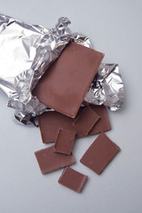 Chocolate Bar Tablet Wrapped in Aluminum Foil over Gray Neutral Background with copy space. Sweet...