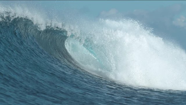 SLOW MOTION, CLOSE UP: Large crystal clear wave breaks on picturesque day at the seaside. Breathtaking ocean wave shines in the blinding summer sunlight and swirls towards the tropical coastline.