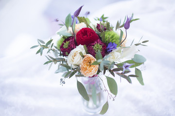Close-up of bouquet with white rose, golden vuvuzela garden rose, violet clematis, green trick carnation, red garden rose, banksia and eucalyptus. Red and white mixed flowers bouquet