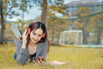 A young teenage student in university smiling and reading the book in summer holiday. She listening the music while reading the book.