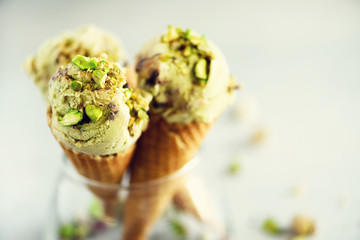 Green ice cream in waffle cone with chocolate and pistachio nuts on grey stone background. Summer...