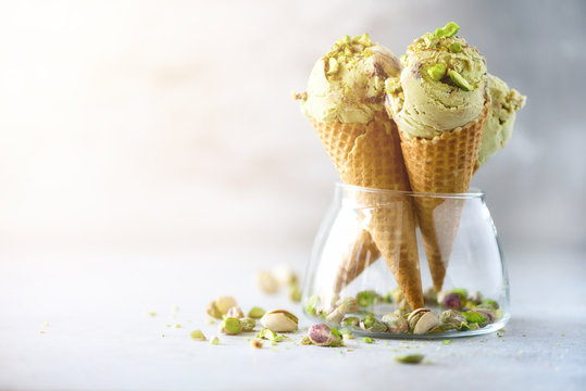 Green ice cream in waffle cone with chocolate and pistachio nuts on grey stone background. Summer food concept, copy space. Healthy gluten free ice-cream.