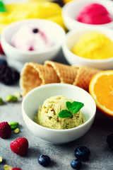 Ice cream balls in bowls, waffle cones, berries, orange, mango, pistachio on grey concrete background. Colorful collection, flat lay, summer concept