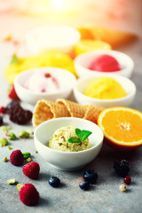 Ice cream balls in bowls, waffle cones, berries, orange, mango, pistachio on grey concrete background. Colorful collection, flat lay, summer concept