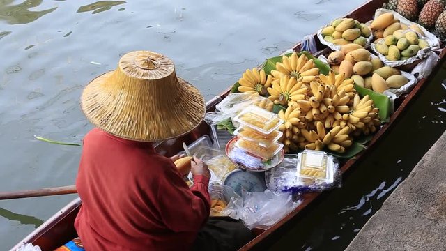 Thai woman on boat with fruits at Damnoen Saduak most famous food floating market . Damnoen Saduak is a very popular tourist attraction in Bangkok, Thailand