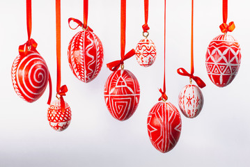 Easter eggs with folk Ukrainian pattern hang on red ribbons from top on white background. Ukrainian traditional eggs pisanka and krashanka. - obrazy, fototapety, plakaty