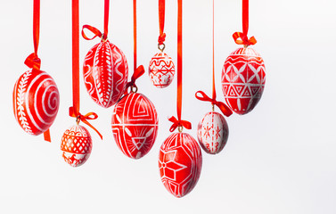 Red easter eggs with folk Ukrainian pattern hang on red ribbons from left side on white background. Ukrainian traditional eggs pisanka and krashanka. - obrazy, fototapety, plakaty