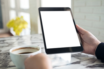 Mockup image of hands holding black tablet pc with white blank screen and coffee cup on table background