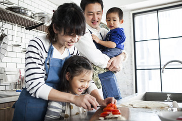 具材を切っているお母さんと娘。お父さんは息子を抱っこしてそれを楽しそうに見ています。